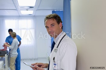 Portrait confident male doctor using digital tablet in hospital room doorway