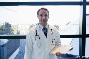 Portrait confident male doctor with clipboard at window in hospital