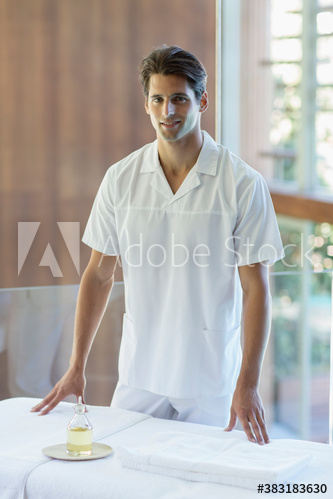 Portrait confident male masseuse standing at spa massage table