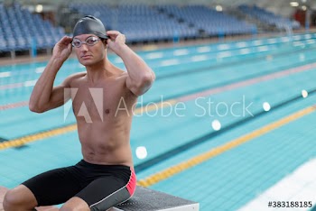 Portrait confident male swimmer on starting block at swimming pool