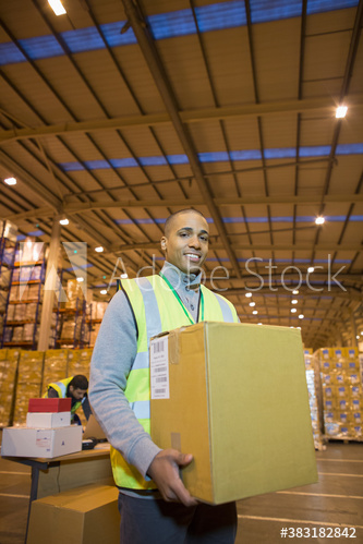 Portrait confident male worker carrying box in distribution warehouse