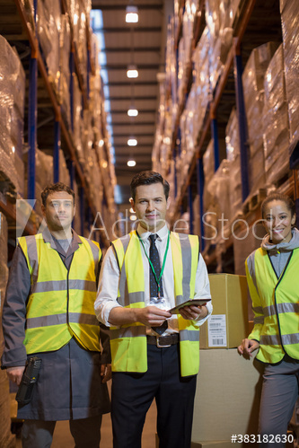 Portrait confident manager and workers in aisle of distribution warehouse