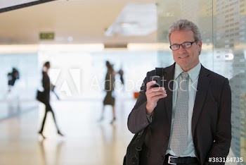 Portrait confident mature businessman using smart phone in corridor
