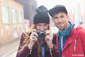Portrait confident young couple with camera on city street