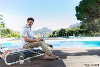Portrait confident young man using laptop at sunny luxury poolside