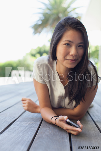 Portrait confident young woman laying on deck with smart phone