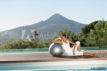 Portrait confident young woman leaning on fitness ball at sunny poolside