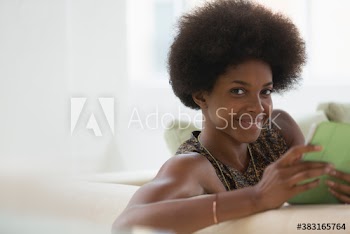 Portrait confident young woman with afro using digital tablet on sofa