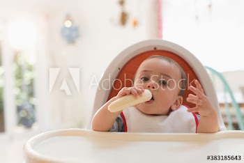 Portrait cute baby boy eating banana in high chair