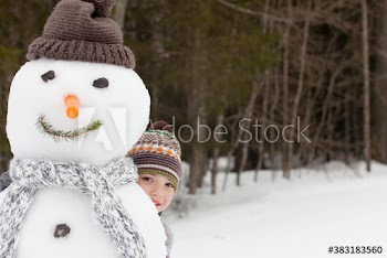 Portrait cute boy hiding behind snowman in snowy woods