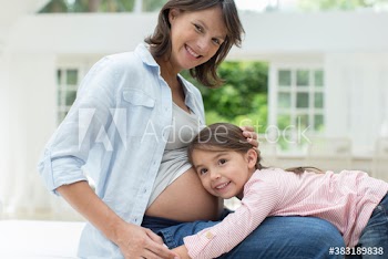 Portrait cute curious daughter listening to stomach of pregnant mother