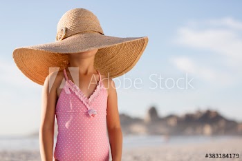 Portrait cute girl in bathing suit and oversized sun hat on sunny beach