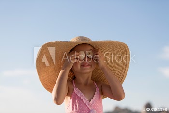 Portrait cute girl in sun hat covering eyes with seashells