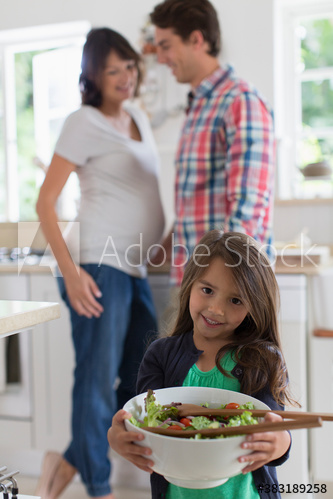 Portrait cute girl with salad and pregnant parents in kitchen