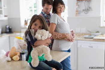 Portrait cute girl with teddy bear and pregnant parents in kitchen