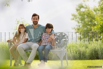 Portrait father and children on bench in sunny backyard