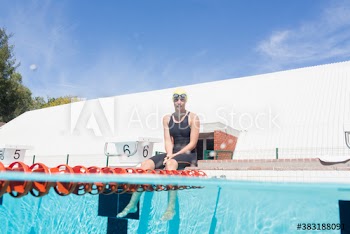 Portrait female swimmer resting at edge of sunny swimming pool