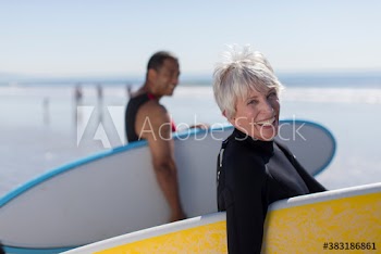 Portrait happy active senior woman with surfboard on sunny beach