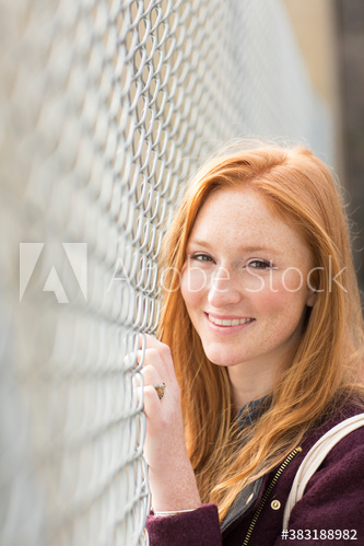 Portrait happy beautiful young woman at sunny chainlink fence
