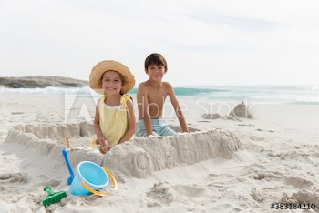 Portrait happy brother and sister building sandcastle on beach