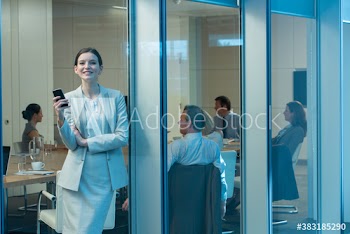 Portrait happy businesswoman with smart phone at office window