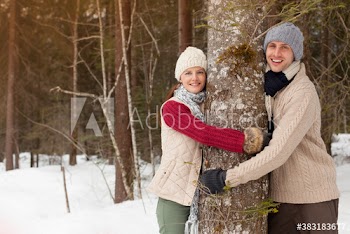 Portrait happy couple tree hugging in snowy woods