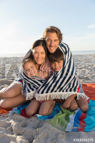 Portrait happy family wrapped in towel on sunny beach