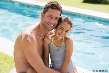 Portrait happy father and daughter hugging at sunny summer poolside