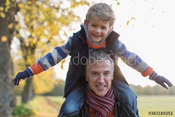 Portrait happy father carrying son on shoulders in autumn park