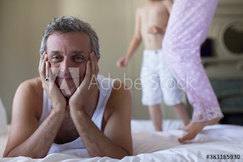 Portrait happy father on bed with jumping kids