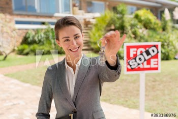 Portrait happy female realtor holding house keys by sold sign
