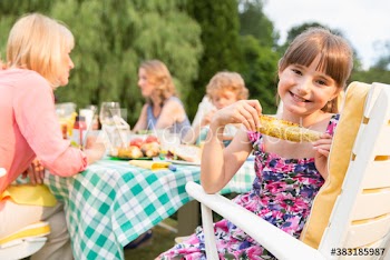 Portrait happy girl enjoying corn on the cob at patio lunch with family