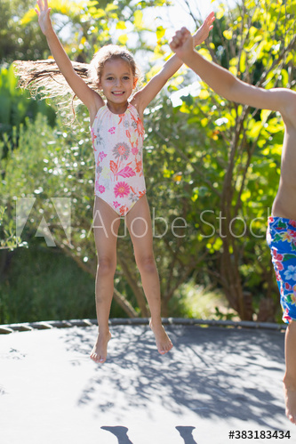 Portrait happy girl in bathing suit jumping on sunny trampoline