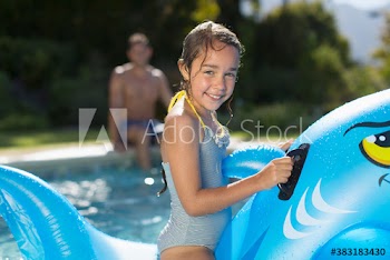 Portrait happy girl on inflatable shark in sunny swimming pool