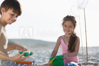 Portrait happy girl playing in sand with brother on sunny beach