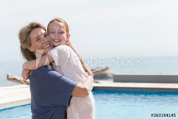 Portrait happy grandmother and granddaughter hugging at sunny poolside