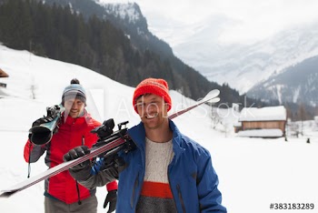 Portrait happy men carrying skis in snow