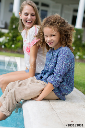Portrait happy mother and daughter dipping legs in swimming pool