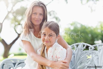 Portrait happy mother and daughter hugging on bench in sunny garden