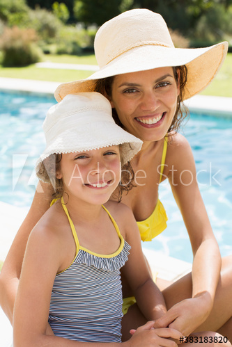 Portrait happy mother and daughter in sun hats at sunny poolside