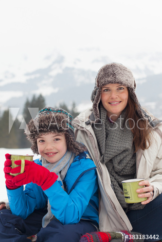 Portrait happy mother and son drinking hot cocoa in snow