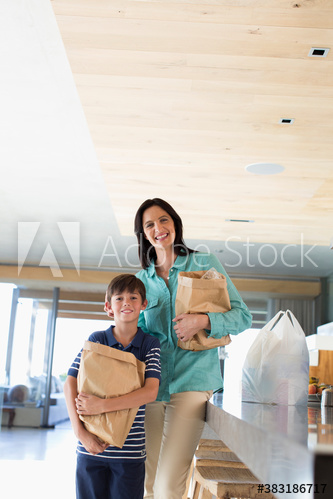 Portrait happy mother and son with grocery bags in kitchen