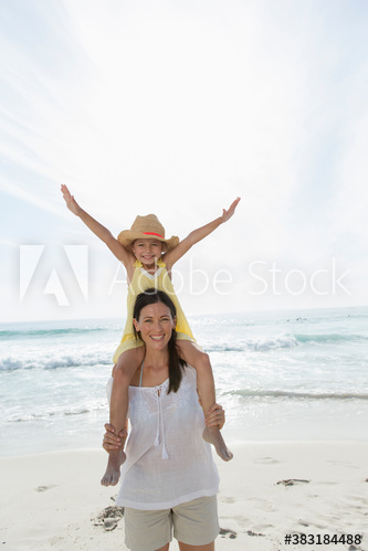 Portrait happy mother carrying daughter on shoulders on sunny beach