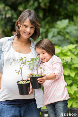 Portrait happy pregnant mother and daughter with saplings