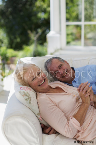 Portrait happy senior couple cuddling on patio sofa