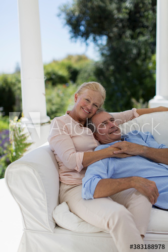 Portrait happy senior couple cuddling on patio sofa