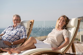 Portrait happy senior couple relaxing on sunny poolside lounge chairs