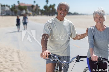Portrait happy senior couple riding bicycles on sunny beach boardwalk