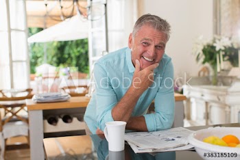 Portrait happy senior man drinking coffee and reading newspaper in kitchen
