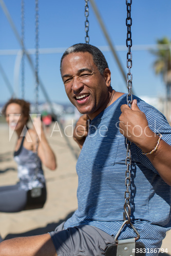 Portrait happy senior man on swing set on sunny beach